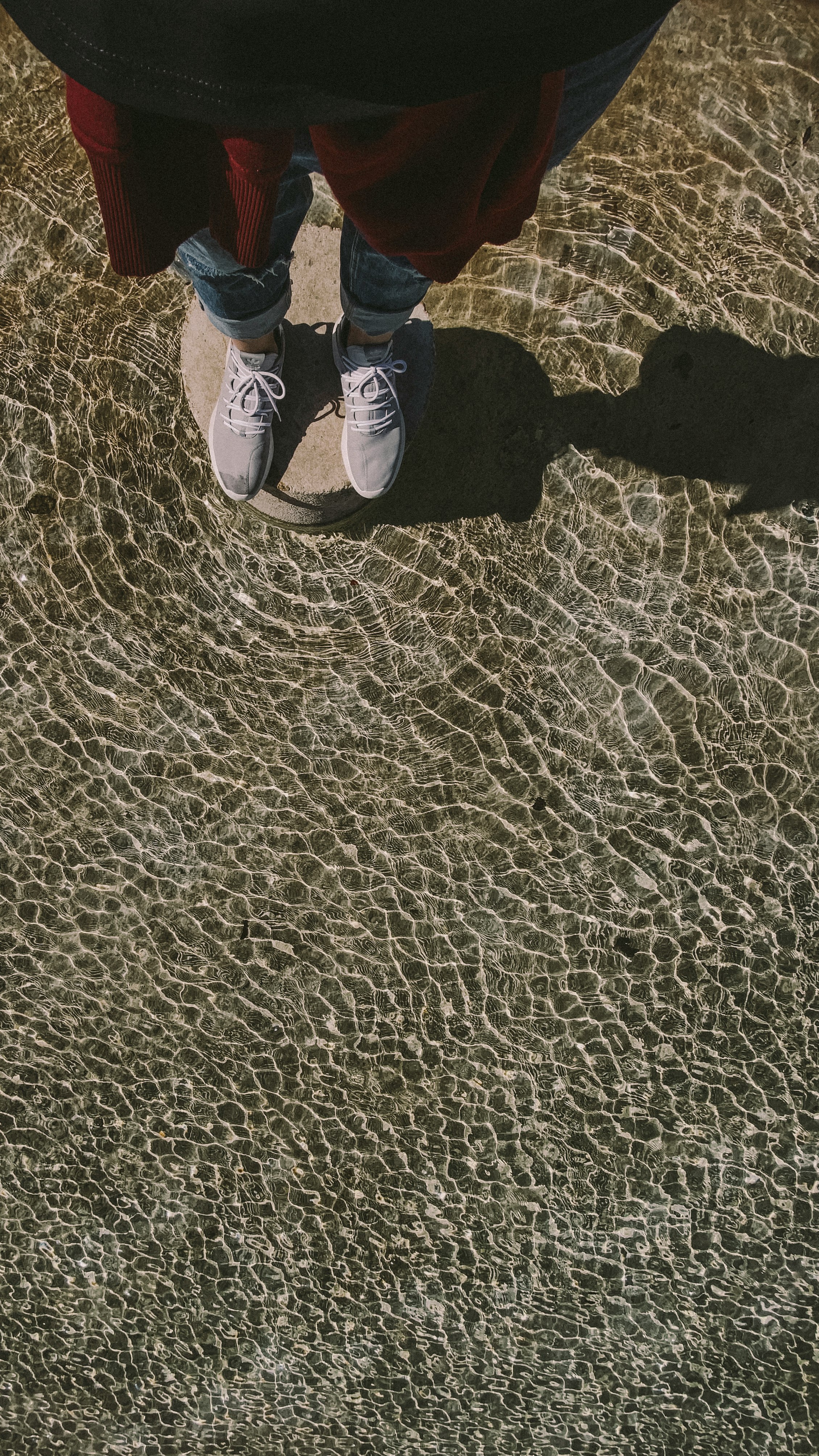 person in blue denim jeans and black shoes standing on brown sand